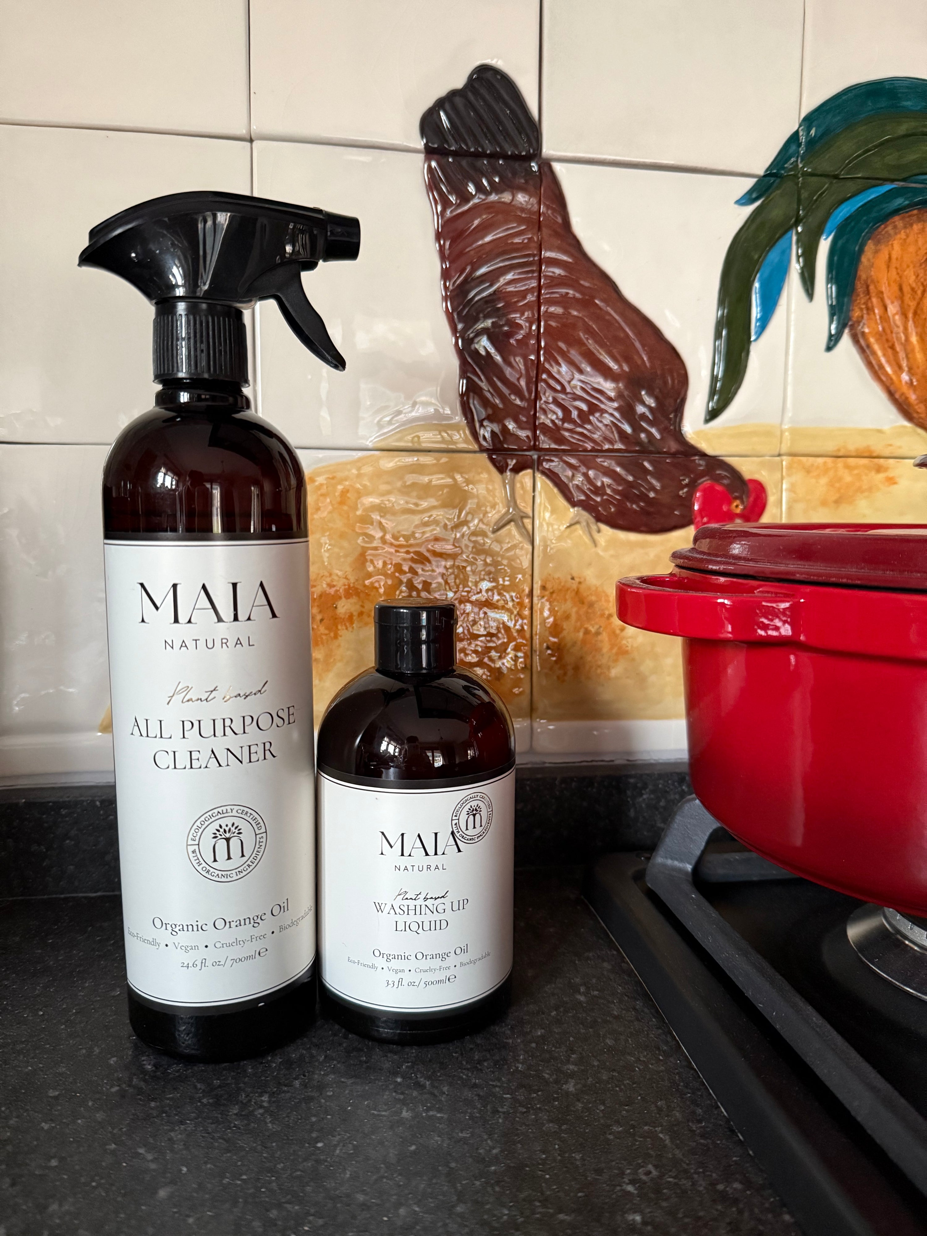 This image features a pair of organic cleaning products from the brand MAIA, displayed on a kitchen counter. The products come in two different sizes, with the larger bottle equipped with a spray nozzle for easy application.